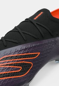 Scarpa da corsa nera e viola con tomaia testurizzata, design elegante e dettagli arancioni. Presenta una chiusura con lacci e una costruzione leggera.