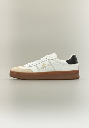 White sneaker featuring a beige suede toe, gold logo detail, black heel accent, and a brown rubber sole. Classic low-top design.