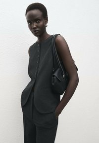 Top sin mangas gris con cierre de botones, combinado con pantalones a juego. Un pequeño bolso negro cuelga del hombro. Textura suave.