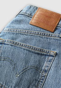 Jeans in denim blu con un'etichetta in pelle marrone, con il logo Levi Strauss visibile. Presentano cuciture in evidenza e una tasca posteriore con un design distintivo.