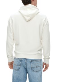 Sudadera de felpa blanca con capucha ajustable, puños y dobladillo acanalados. Se lleva con unos vaqueros de denim azul claro que presentan detalles de costura en los bolsillos traseros.