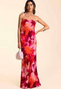 Robe de soirée sans bretelles ornée de motifs floraux, présentant un dégradé de teintes roses, rouges et oranges avec une silhouette élégante. Associée à un petit sac à main rose.