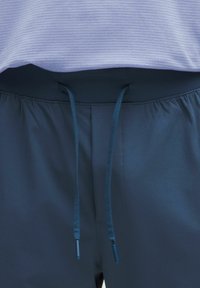 Jūriniai sportiniai kelnės su raišteliu liemens. Minkšta, lygi medžiaga su švelniu blizgesiu. Užpildyta liemens juosta užtikrina patogumą.