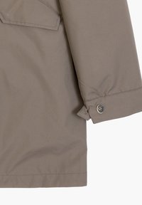 Giacca impermeabile khaki con una texture liscia, polsini con bottone e tasca laterale con pattina inclinata, che mette in mostra un design minimalista.
