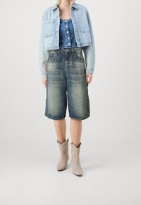 Jasnoniebieska krótka kurtka dżinsowa z dwoma kieszeniami, zestawiona z dopasowanym niebieskim body dżinsowym oraz dzianinowymi spodniami dżinsowymi o średniej długości i wyblakłym efekcie. Beżowe kowbojskie buty.