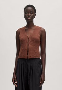 Brauner gestrickter Weste mit strukturiertem Finish, V-Ausschnitt und einer Knopfverschluss vorne, kombiniert mit schwarzen plissierten Hosen.