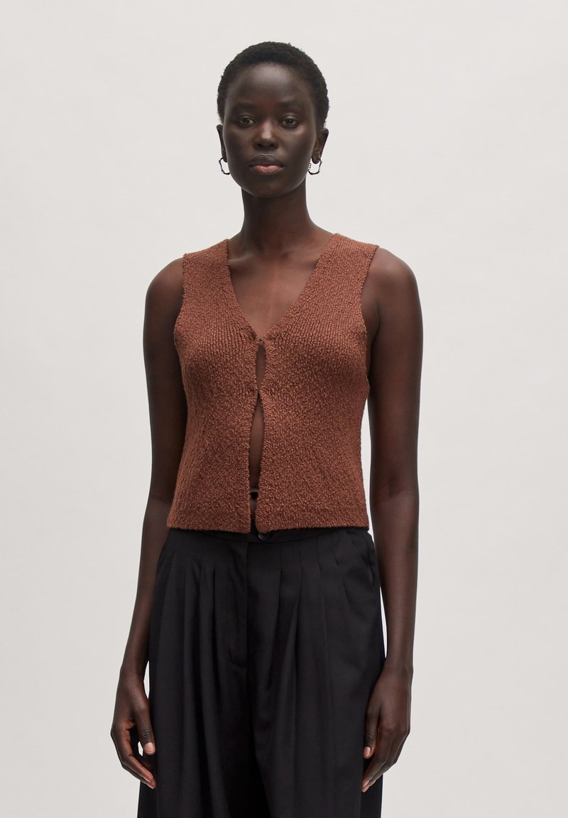 Brauner gestrickter Weste mit strukturiertem Finish, V-Ausschnitt und einer Knopfverschluss vorne, kombiniert mit schwarzen plissierten Hosen.