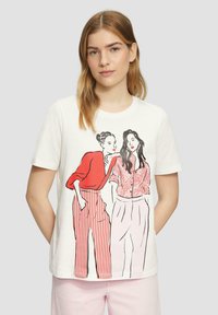 T-shirt blanc avec un imprimé graphique de deux femmes ; l'une en rouge avec un pantalon rayé, l'autre en fleurs, en tissu léger et doux avec des manches courtes.