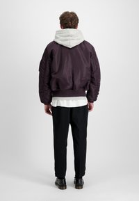 Violeta bomber jaka ar pelēku kapuci, ribotām aprocēm un apakšmalu. Melni bikses un melnas kurpes papildina tērpu. Minimālistisks dizains.
