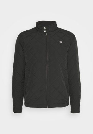 Black quilted jacket featuring a high collar, zip front, two snap buttons, and a small logo on the left chest. Soft, textured fabric.