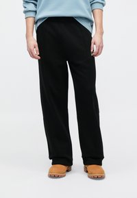 Μαύρη φόρμα με άνετη εφαρμογή, που διαθέτει πλαϊνές τσέπες και διακριτικές λεπτομέρειες ραφής. Φορεμένη με ταμπά μπότες χωρίς κορδόνια.