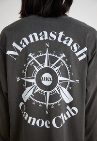 Gray sweatshirt featuring a white compass design with the text "Manastash Canoe Club" and "mcc" in a circular layout on the back.