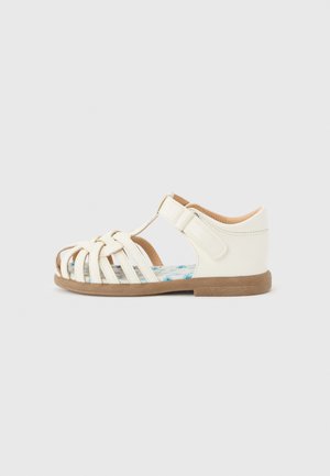 Sandale blanche fermée pour tout-petit avec des sangles tissées, une semelle intérieure à motif floral, une bride de cheville réglable en Velcro et une semelle plate marron.