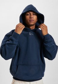 Sudadera con capucha de color marino hecha de una tela texturizada, con un bolsillo tipo canguro y un logo blanco bordado en el pecho, que presenta un ajuste relajado.