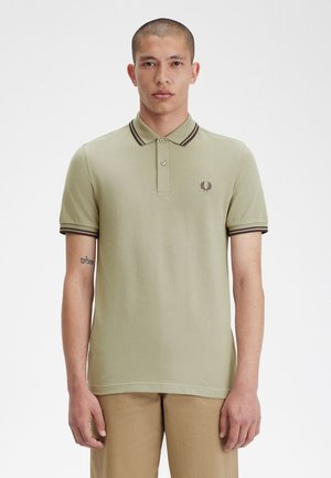 Camisa polo verde caqui con cuello, tapeta de dos botones y ribete en marrón oscuro contrastante en las mangas y el cuello; logo bordado en el pecho.