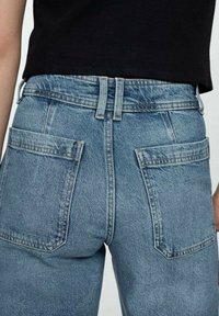 Vaqueros de mezclilla azul claro con cintura alta, corte recto y dos bolsillos traseros. Presentan costuras visibles y presillas para cinturón.