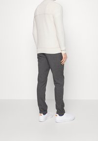 Light beige sweater with a textured pattern, paired with dark gray trousers and white sneakers featuring orange accents.