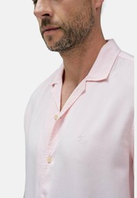 Lichtroze kortarmshirt met een kraag, voorzien van een knoopsluiting en een klein geborduurd logo op de borst. Glad textuur.