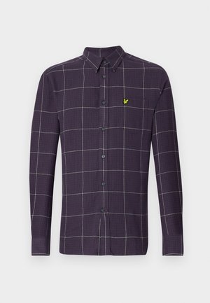 Long-sleeve button-up shirt in dark purple with a grid pattern in white and grey. Features a small, green emblem on the chest pocket.