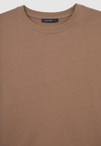 Maglietta a maniche corte marrone a girocollo con colletto cucito e un piccolo etichetta nera all'interno del collo che riporta la scritta "CALLIOPE S".