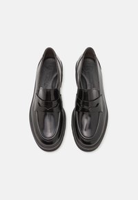 Mocassini in pelle nera dal design elegante, caratterizzati da un accento a fiocco rialzato e una texture liscia, completati da una robusta suola in gomma.