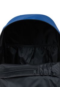 Blå ryggsäck med svart inredning, en dragkedjefack och ett mesh-fack. Har ett slätt tygutsida och en rymlig design.