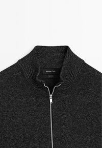 Sweatshirt zippé en coton gris foncé avec un col côtelé et des éléments en métal pour la fermeture. Présente un motif de tricot texturé, étiquette visible à l'intérieur.