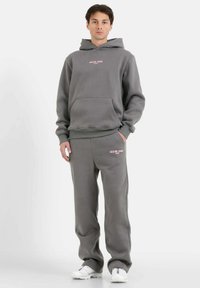 Sudadera gris y pantalones de chándal a juego, confeccionados con una tela suave. La sudadera cuenta con un bolsillo frontal y texto del logo en rosa. Ajuste casual y relajado.