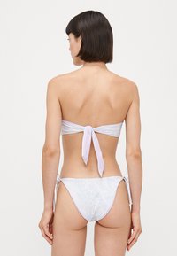 Bikini set featuring a strapless top with a tie at the back, and patterned hipster bottoms in pastel colors with side ties.