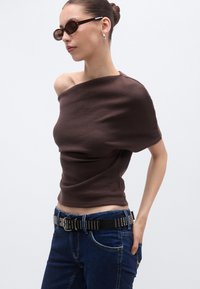Καφέ κοντό τοπ με ντεκολτέ που αφήνει τους ώμους ακάλυπτους, με λεία υφή. Συνδυάζεται με μπλε τζιν και μαύρη ζώνη με τρουκς και ασημένιες λεπτομέρειες.