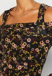 Černé květinové šaty s nařasenou texturou; vzor malých bílých, vínových a oranžových květin na zeleném listovém podkladu. Čtvercový výstřih.