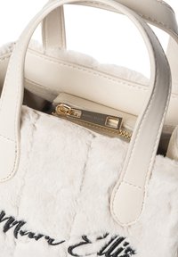 Borsa a mano in pelliccia sintetica color crema con manici in pelle, dotata di una zip dorata e del nome del marchio "Marc Ellis" impresso all'interno. Gli accenti includono un ricamo nero.