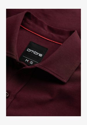 Bordeaux katoenen overhemd met een kraag, voorzien van contrasterende rode stiksels en een zwart label met de tekst "ombre," maat M, stijlkenmerken zichtbaar.