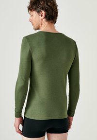 Langarmshirt in olijfgroen, aansluitend ontwerp, gemaakt van zachte stof, met een ronde halslijn en geribbelde manchetten, gedragen met zwarte boxershorts.