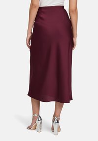 Bordeauxfarbene Satin-Midikleid mit einer glatten Textur, ausgestattet mit einem taillierten Bund und einem dezenten Fluss bis zum Saum. Silberne Absatzsandalen.