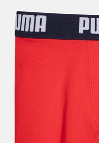 Rde bombažne bokserice z mornarsko modrim pasom, ki vsebujejo belo blagovno znamko "PUMA". Gladka tekstura in oprijet dizajn, ki poudarjata udobje.