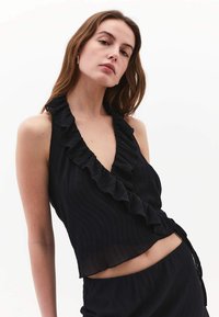 Top nero con scollo a oblò e rifiniture a volant, realizzato in tessuto testurizzato. Il design è aderente, con un davanti sovrapposto e una lunghezza cropped.
