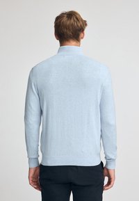 Ljusblåa tröja i mjukt tyg, med hög krage, långa ärmar samt ribbade manschetter och nederkant. Slät textur.