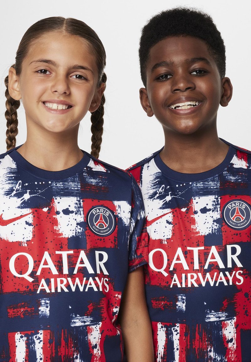 Zwei Kinder tragen marineblaue und rote Fußballtrikots. Die Shirts haben ein Farbspritzer-Muster, das Nike-Logo und den Text "Qatar Airways".