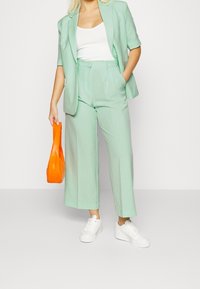 Blazer ajusté vert menthe clair à manches courtes, pantalon large assorti et débardeur blanc ; accessoirisé avec un sac à main orange.