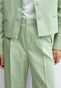 Lichtgroen op maat gemaakt pak met een slim-fit blazer met twee knopen en bijpassende high-waisted broeken met plooien. Gestructureerde stof.