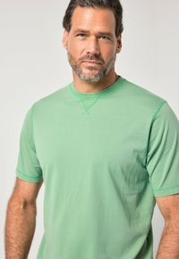 Zelené tričko s krátkými rukávy vyrobené z měkké látky, s kulatým výstřihem a kontrastními švy. Jednoduchý design bez vzorů.