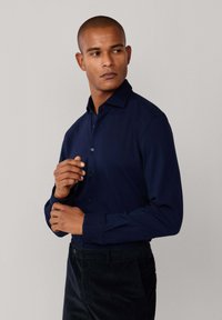 Marineblauwe overhemdd met kraag en lange mouwen, met een gladde textuur en subtiele glans, gecombineerd met donkere pantalons.