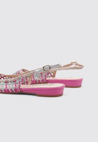 Sandalias planas con un empeine tejido en rosa, blanco y gris, que presentan una correa con hebilla y una suela rosa sólida.