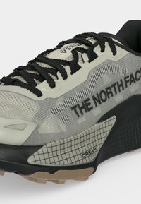 Baskets North Face gris clair et noir avec lacets noirs, tige en mesh et semelle texturée affichant le texte "DREAM" près du talon.