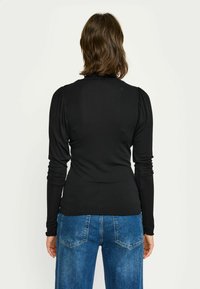 Črni dolgi rokav s podrobnostmi gubanih ramen, prilegajoča silhueta in raztegljiv material, v kombinaciji z svetlo pranimi jeans hlačami.