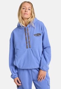 Haut en polaire bleu avec un col à cordon, des détails de motif tribal et un logo à l'avant. Présente une coupe décontractée et des poignets côtelés.