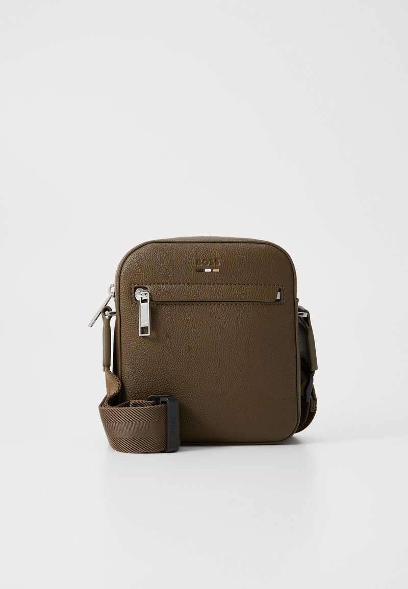 Brun lædercrossbody taske med en tekstureret finish, frontlomme med lynlås, sølvfarvet hardware og justerbar rem. Kompakt firkantet form.