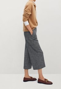 Beżowy sweter dzianinowy, szare szerokie spodnie w kratę oraz brązowe mokasyny z złotymi akcentami. Teksturowana tkanina i luźny krój.
