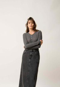 Szary sweter z prążkowanego dzianiny z dekoltem w serek i zapięciem na guziki, zestawiony z czarną spódnicą dżinsową o wysokim stanie z bocznymi kieszeniami i rozcięciem z przodu.